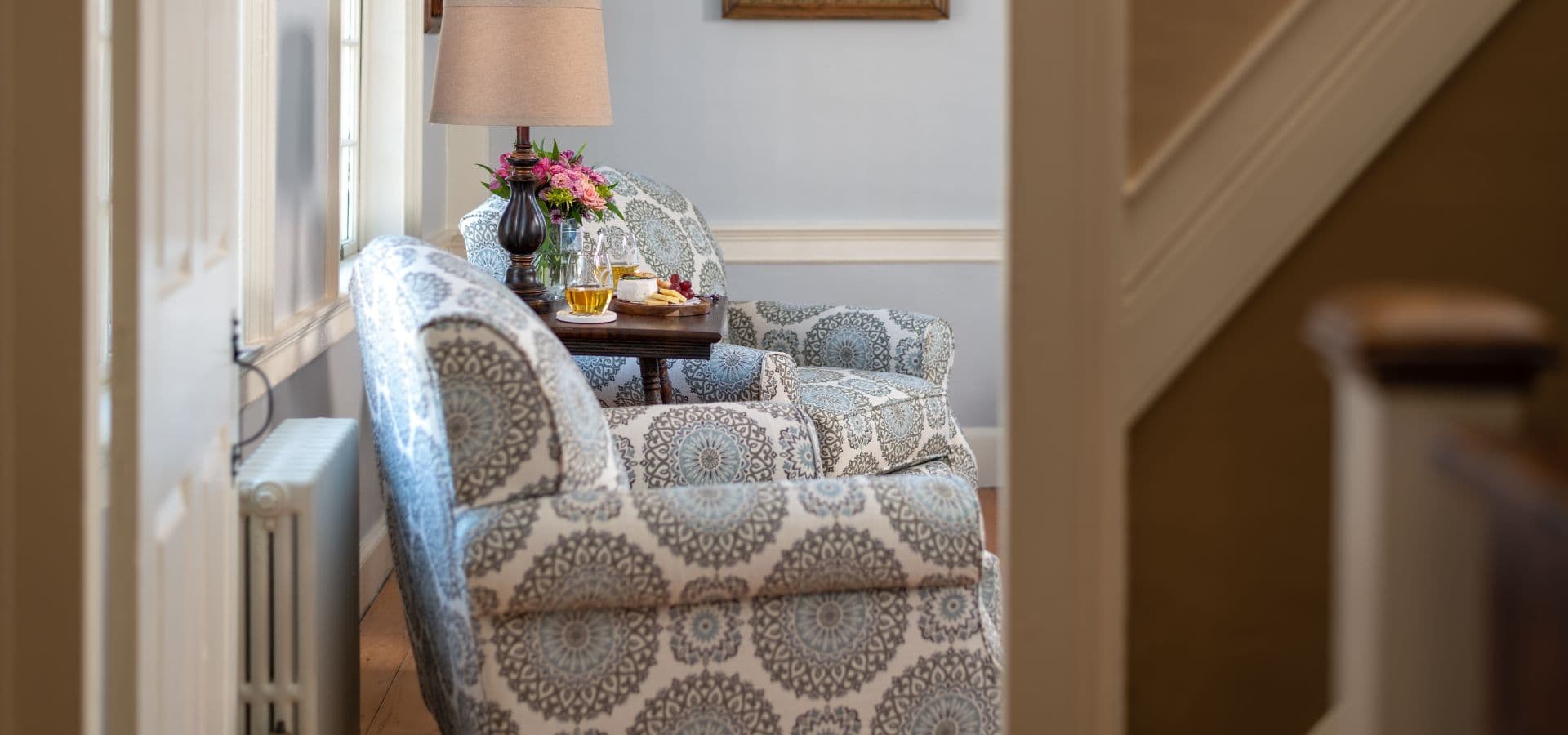 Cozy seating area with patterned chairs, a small table, and a lamp beside a staircase.