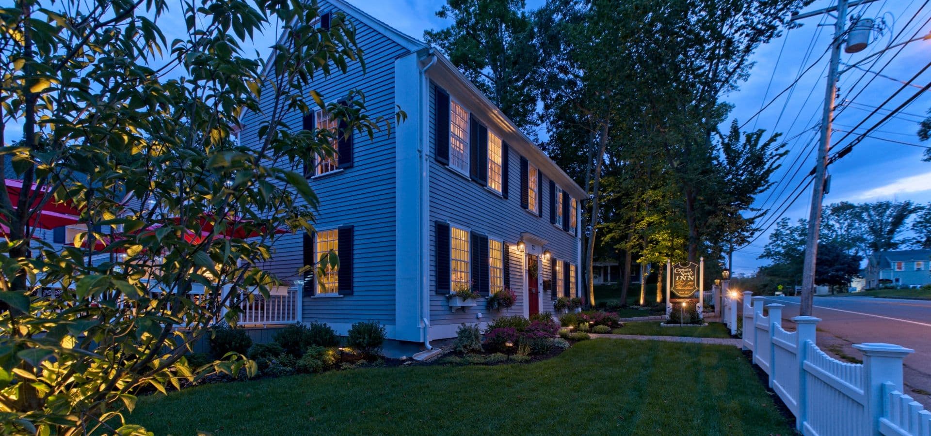 A charming blue house with illuminated windows surrounded by greenery at dusk.