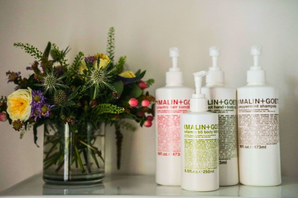 A vase of colorful flowers beside a collection of Malin+Goetz hair and body care products.