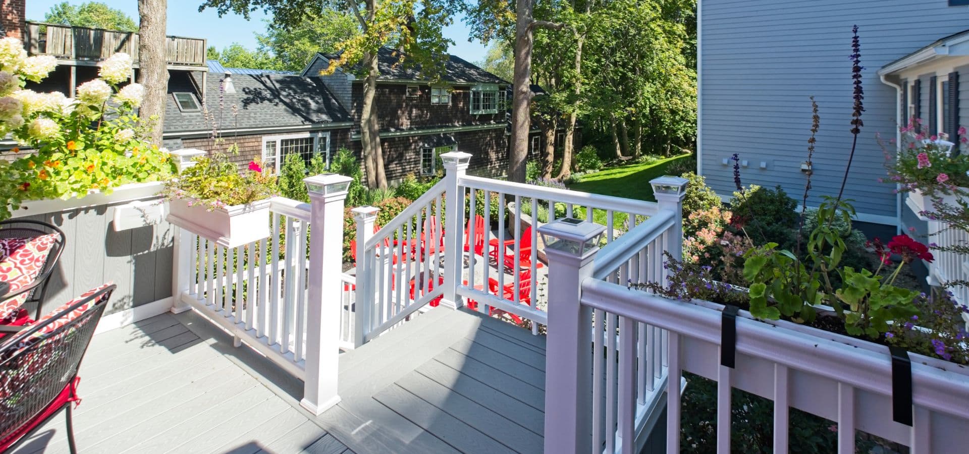 A sunlit deck with white railings and vibrant plants, leading to a spacious outdoor area.