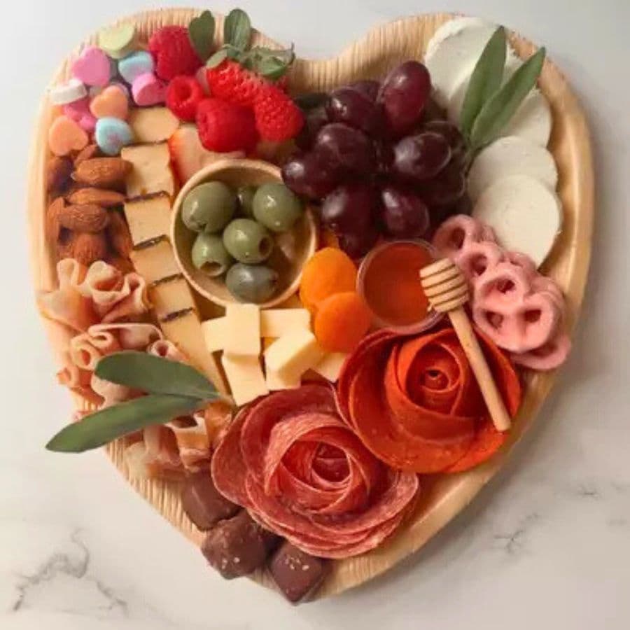 A heart-shaped charcuterie board featuring assorted meats, cheeses, fruits, nuts, and sweets.