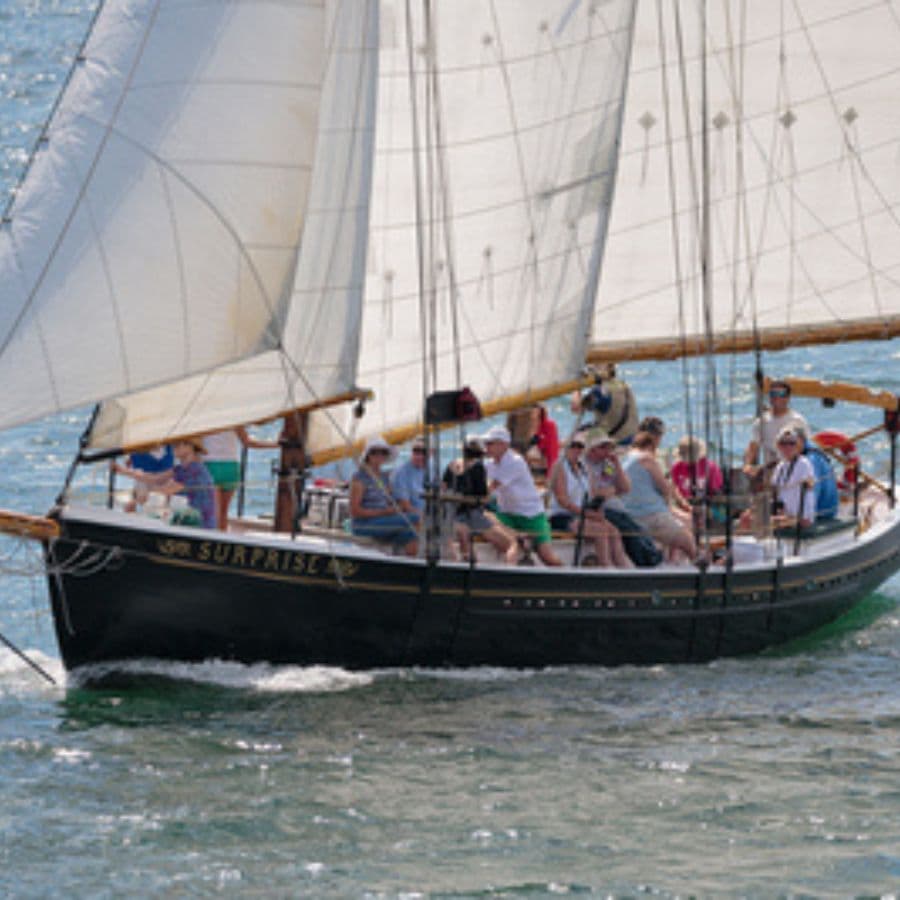A large sailing vessel named "Surprise" with multiple passengers on board navigating through the water.
