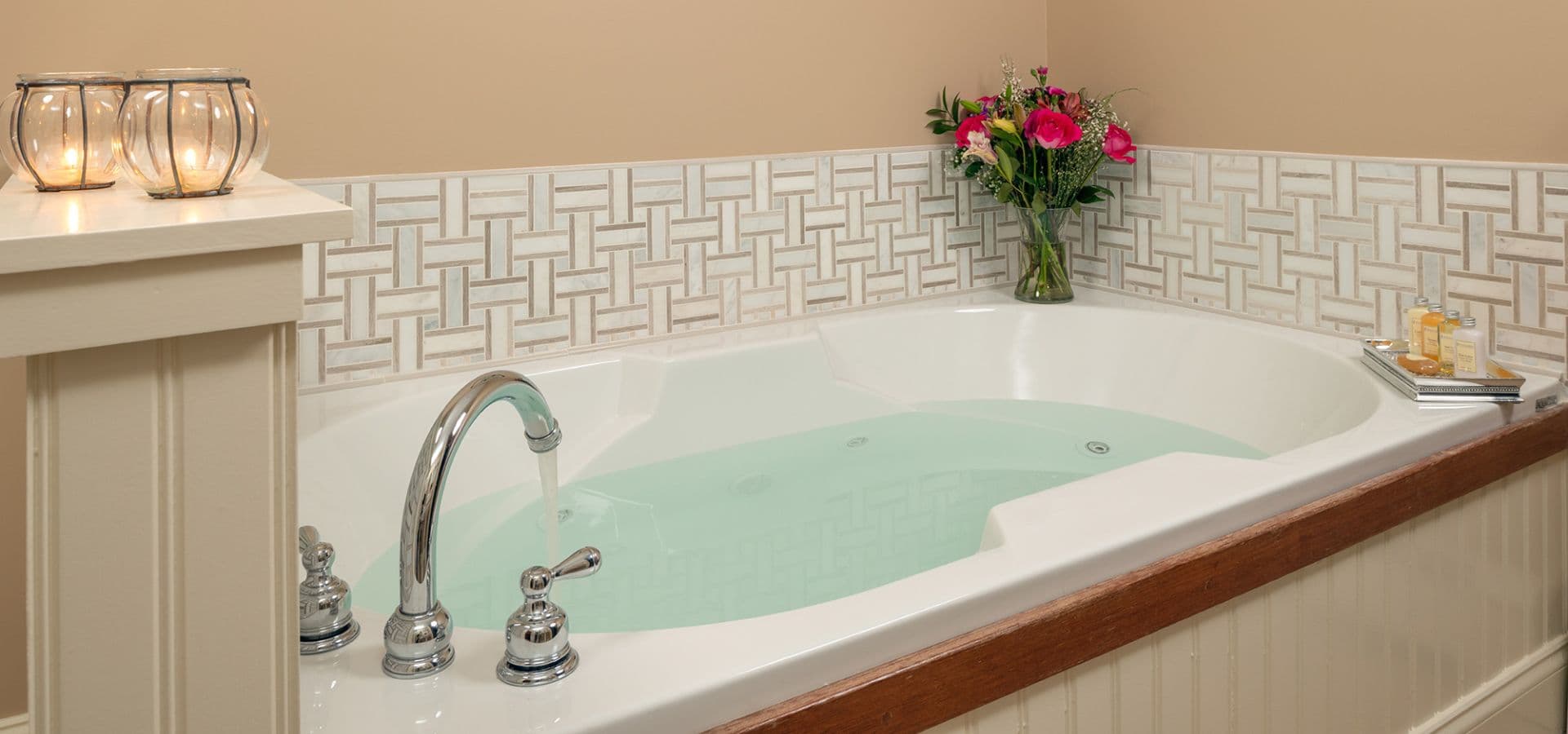 A luxurious soaking tub with light green water, surrounded by decorative tiles and fresh flowers.