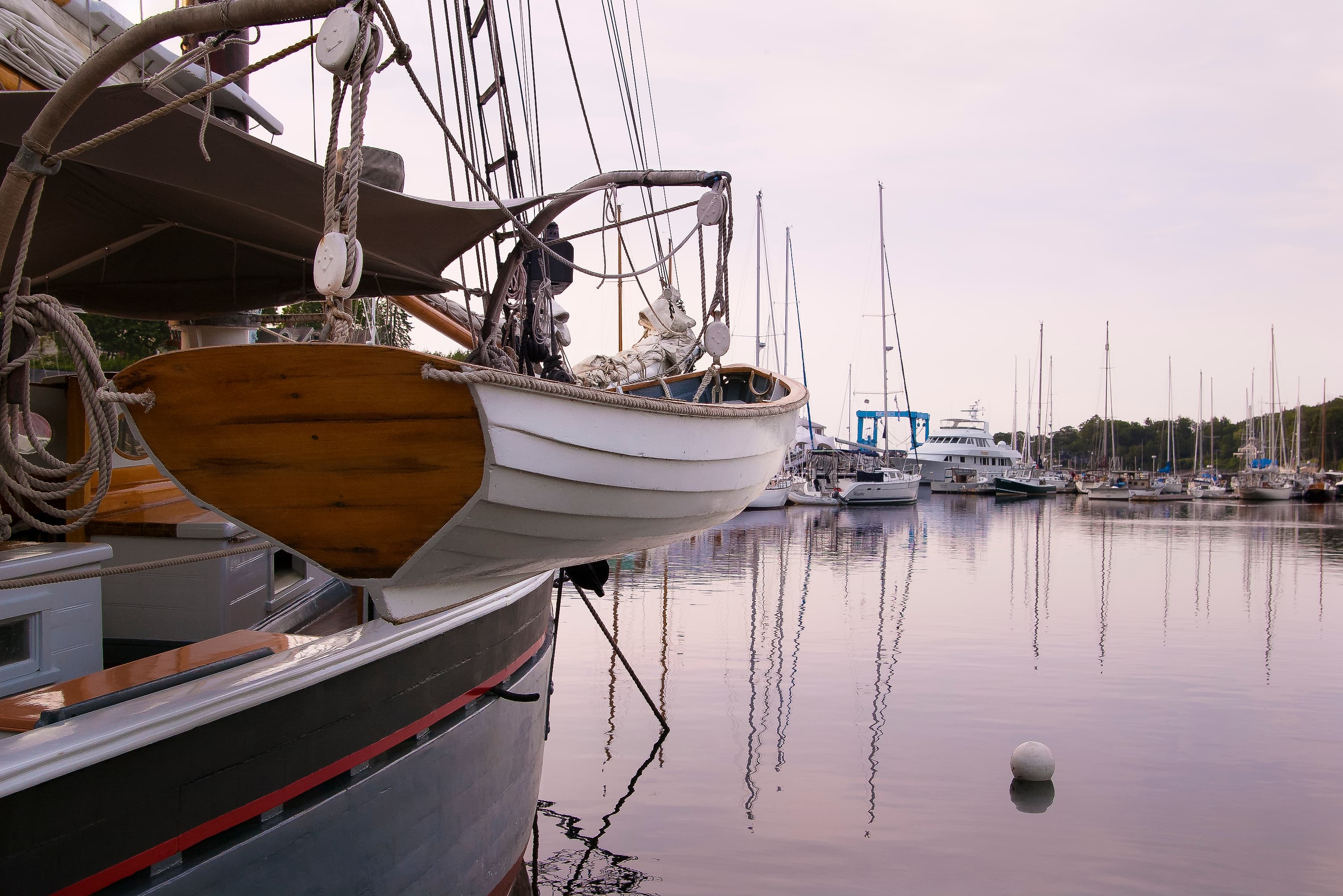 A wooden boat is moored at a tranquil marina surrounded by sailboats and reflections in the water.