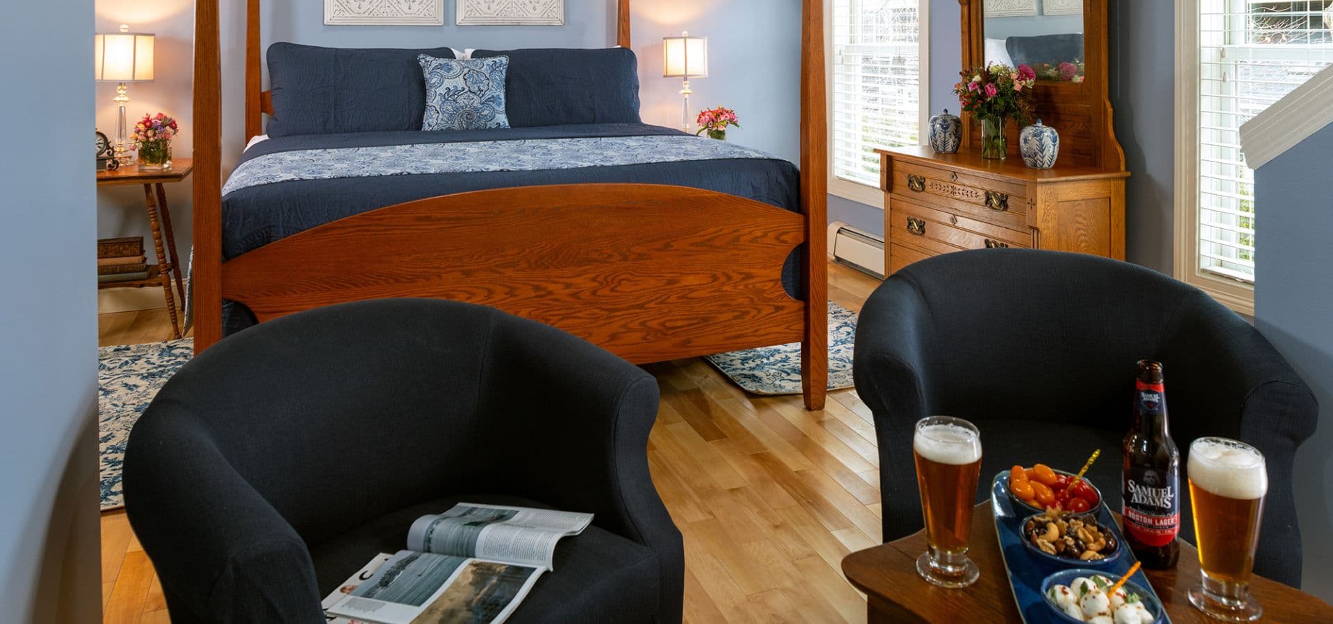 A cozy bedroom with a wooden bed, two armchairs, and a small table set with drinks and snacks.