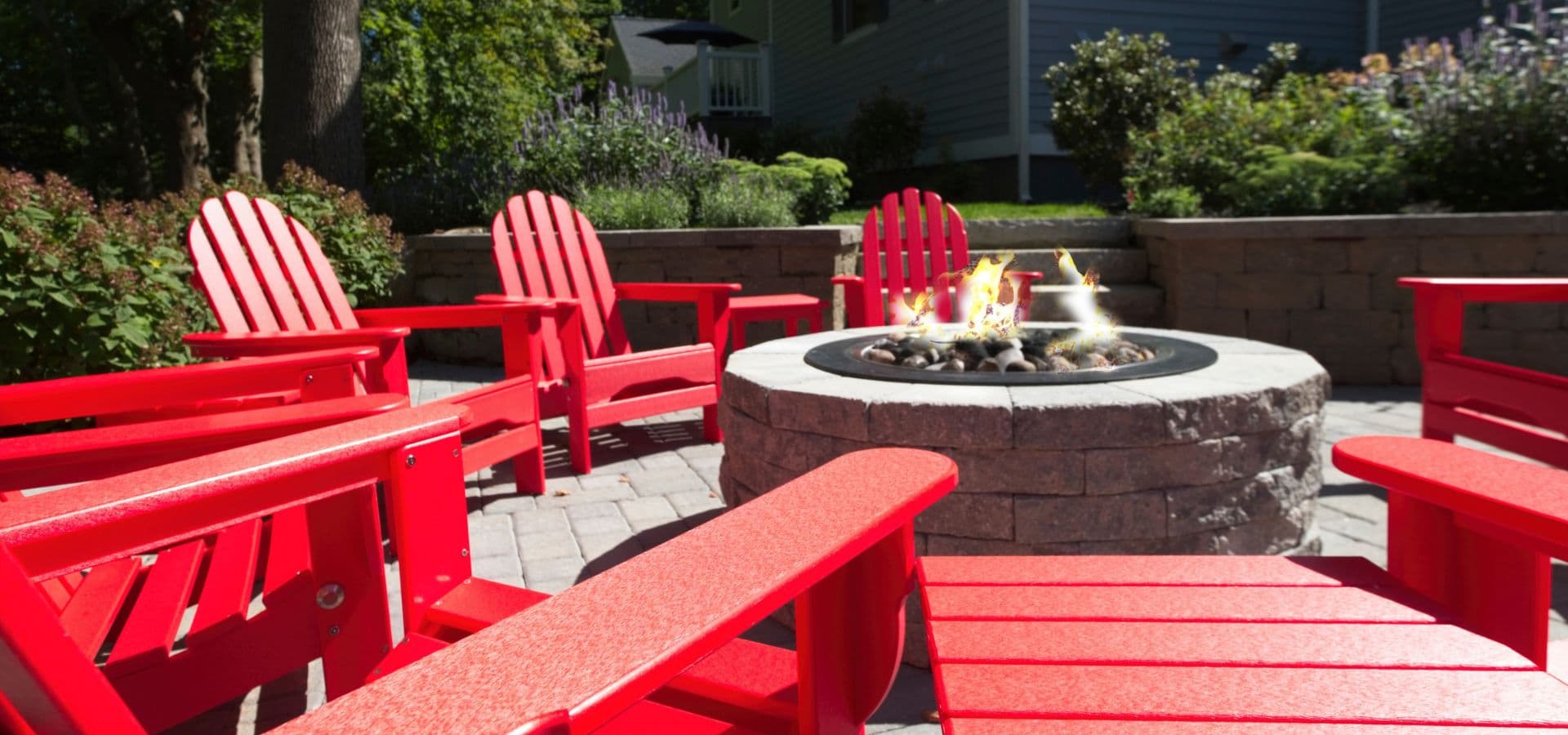 A cozy outdoor seating area featuring red Adirondack chairs around a stone fire pit.