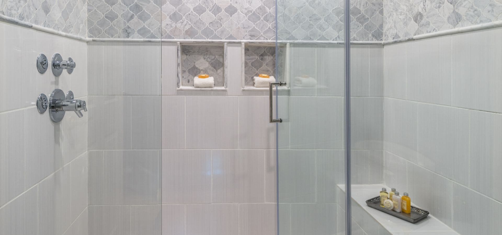 A modern shower featuring gray tiles, glass enclosure, and built-in shelves with toiletries.