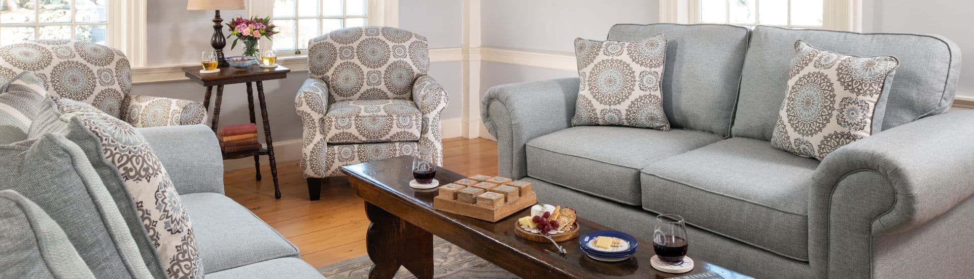 Living room featuring a gray sofa, patterned armchairs, and a wooden coffee table with snacks.