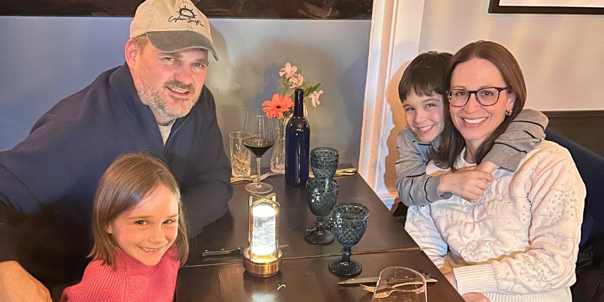 A family of four sits together at a table in a cozy restaurant, smiling and enjoying their meal.