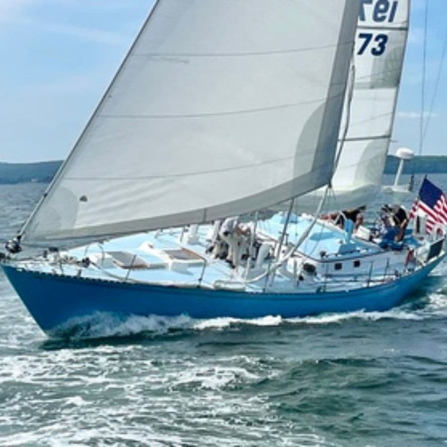 A blue sailboat with an American flag sails through choppy water under a clear sky.