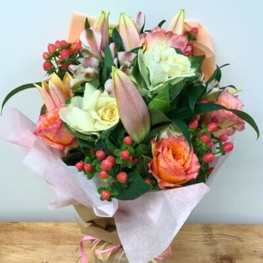 A vibrant bouquet of mixed flowers, including pink lilies and roses, arranged with greenery and berries.