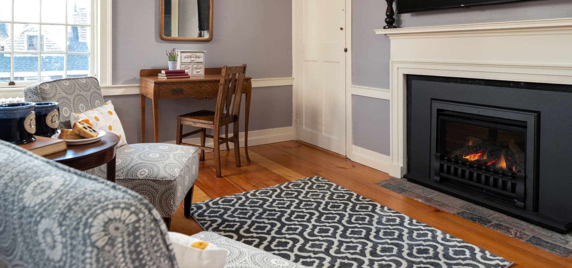Cozy living room featuring a fireplace, patterned rug, a small desk, and comfortable seating.