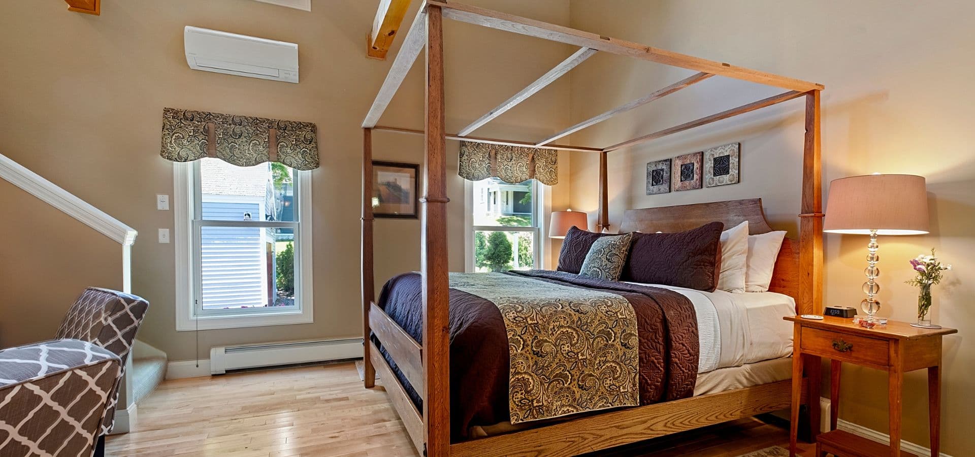 Cozy bedroom featuring a four-poster bed, wooden flooring, and a bright window.