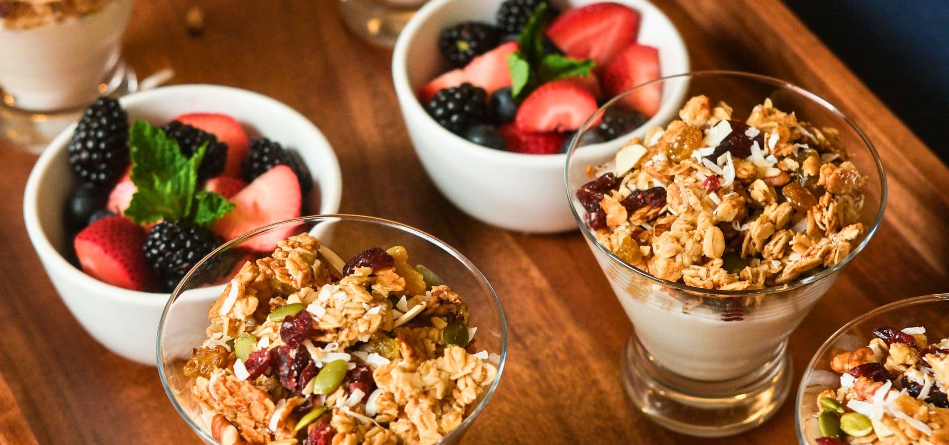 A wooden tray displays yogurt parfaits topped with granola and bowls of fresh berries.