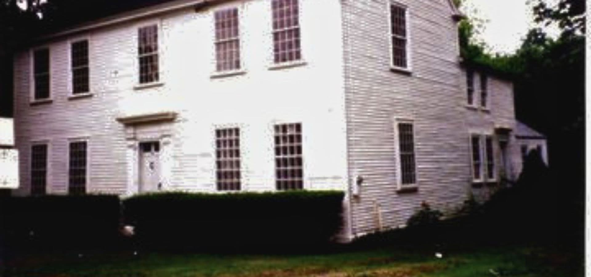 A white two-story house surrounded by greenery.