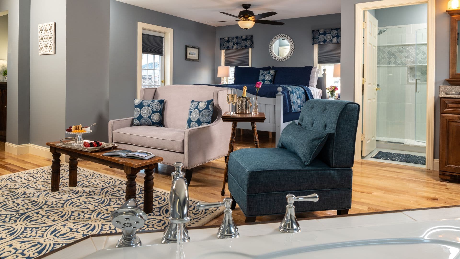 A cozy living space featuring a stylish sofa, armchair, coffee table with snacks, and a view of a bathroom.