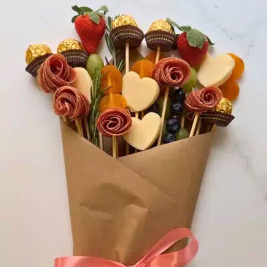 A bouquet made of various candies, fruits, and snacks arranged in a paper cone with a pink ribbon.