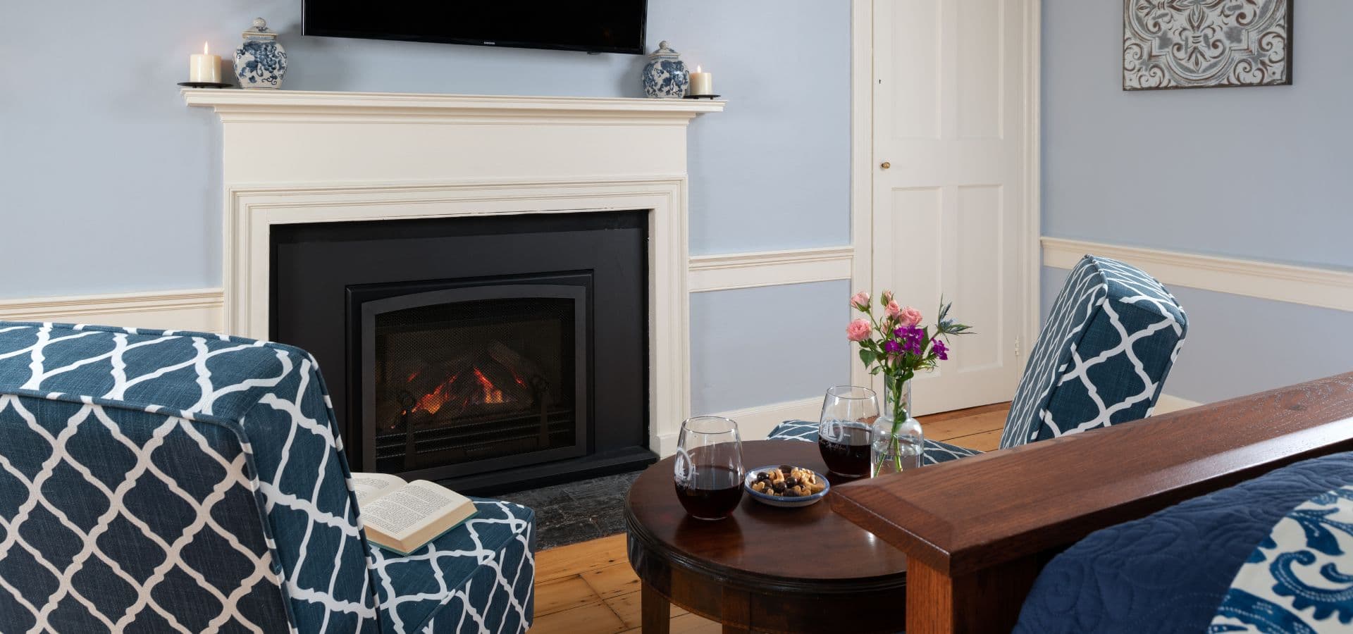 Cozy living room featuring a fireplace, blue walls, and comfortable seating with wine glasses and flowers on a table.