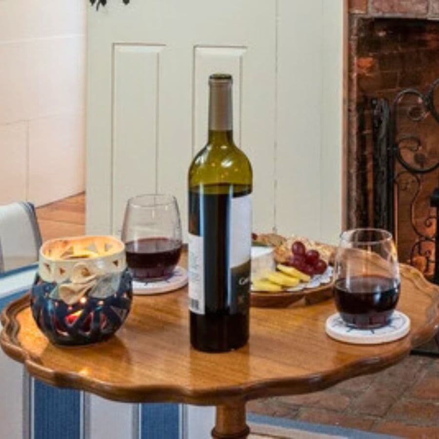 A table with a bottle of red wine, two glasses, a candle, and a small plate of fruit.