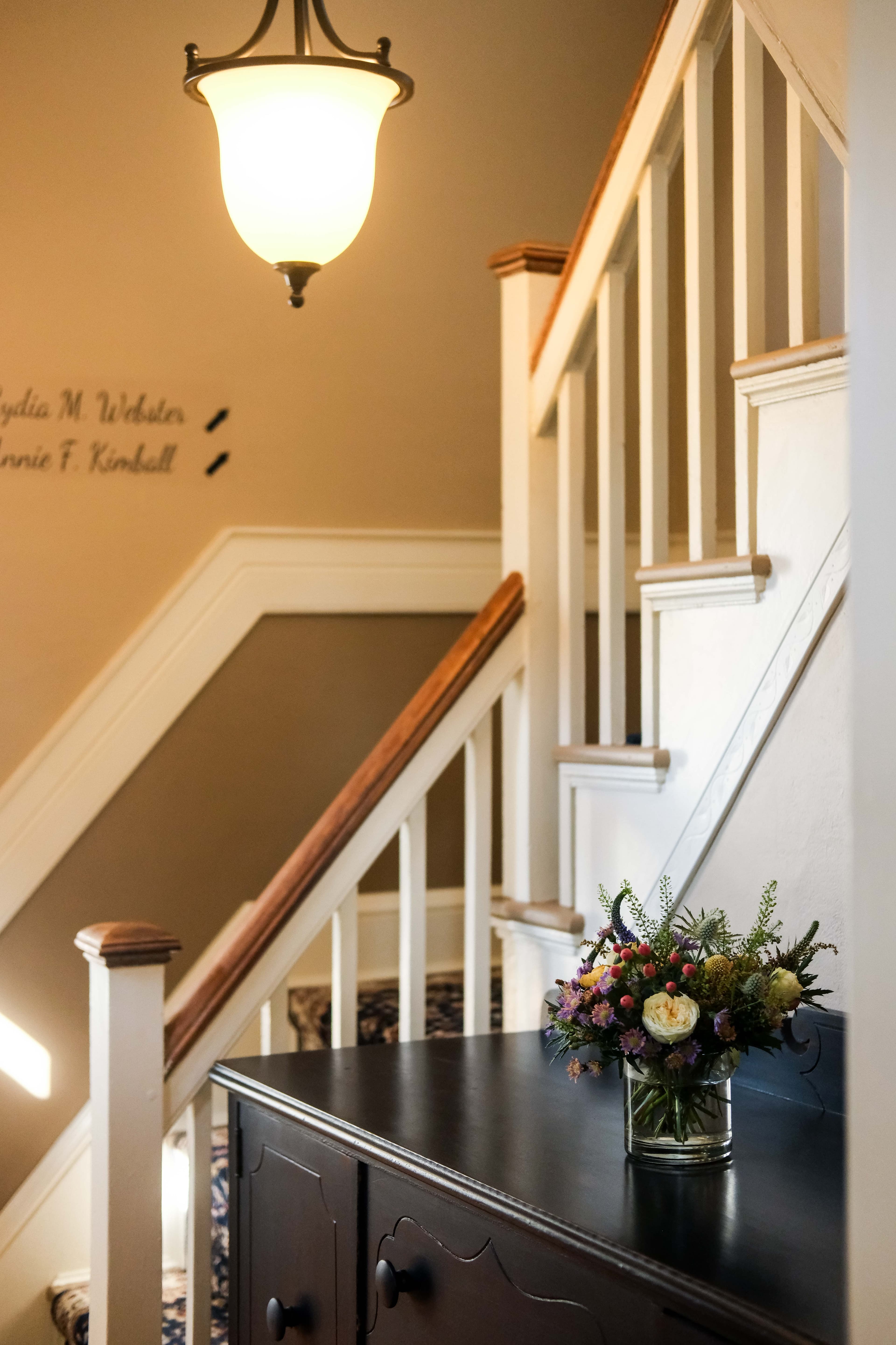 A well-lit staircase with a wooden railing and a small floral arrangement on a dark cabinet.