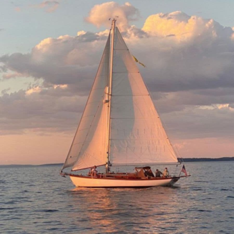A sailboat glides across calm waters under a pink and orange sky.