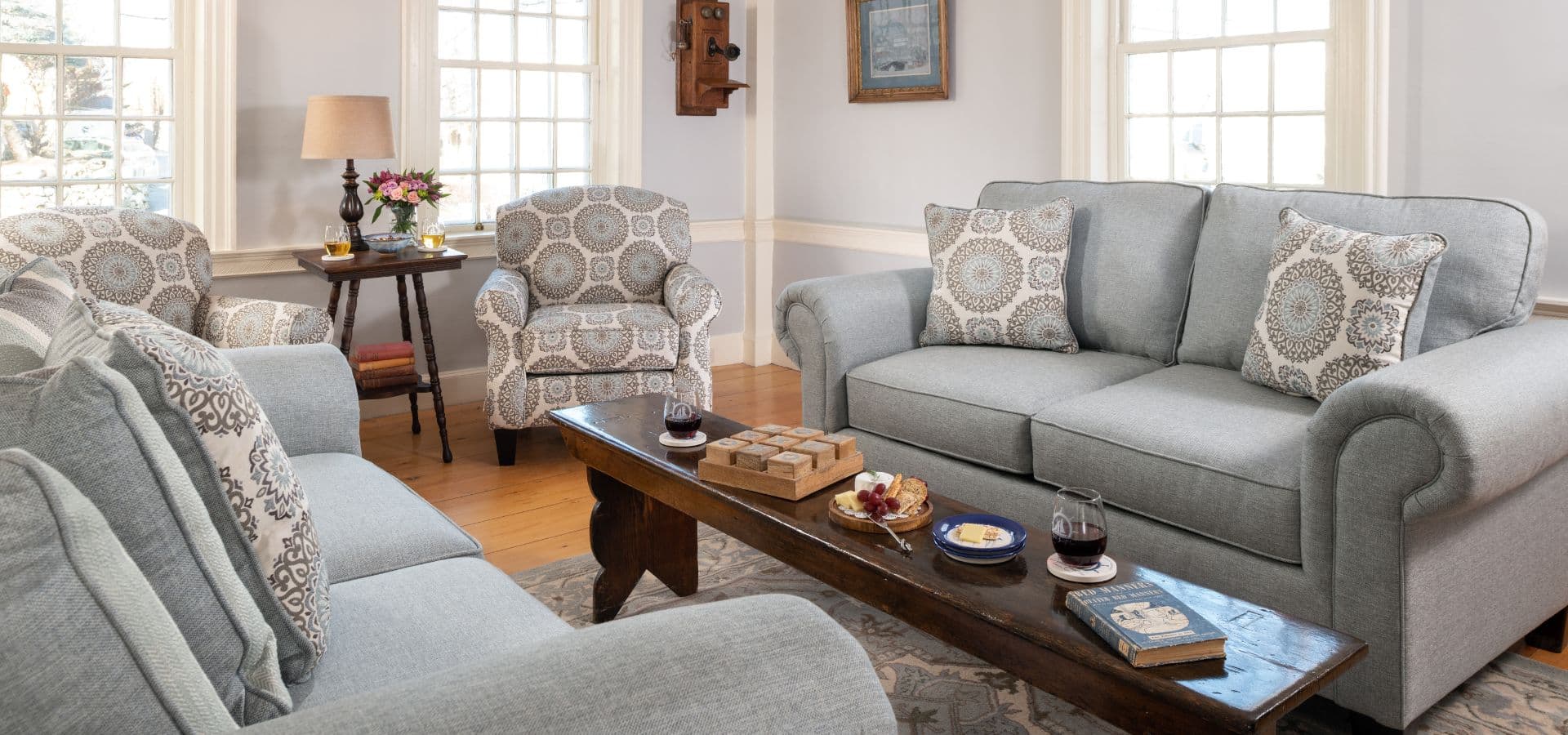 A cozy living room featuring a gray sofa, patterned armchairs, and a wooden coffee table with snacks and drinks.
