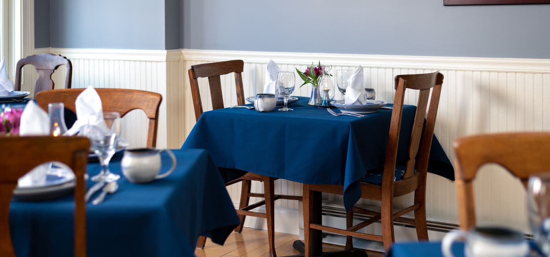 A cozy dining area with blue tablecloths, wooden chairs, and elegantly set tables.