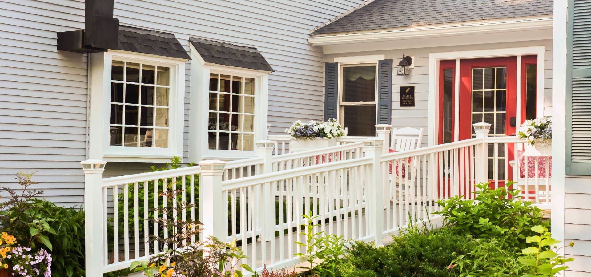 A welcoming house entrance with a white railing, red door, and flowerbeds.
