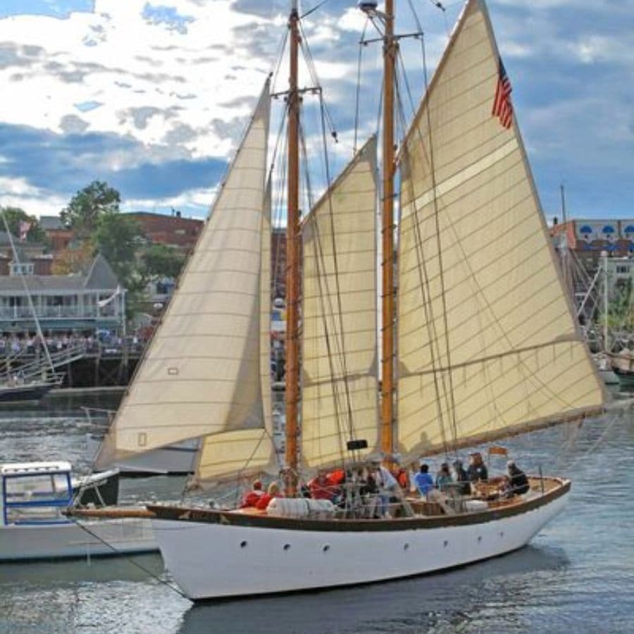 A sailing ship with large white sails navigates a calm harbor.