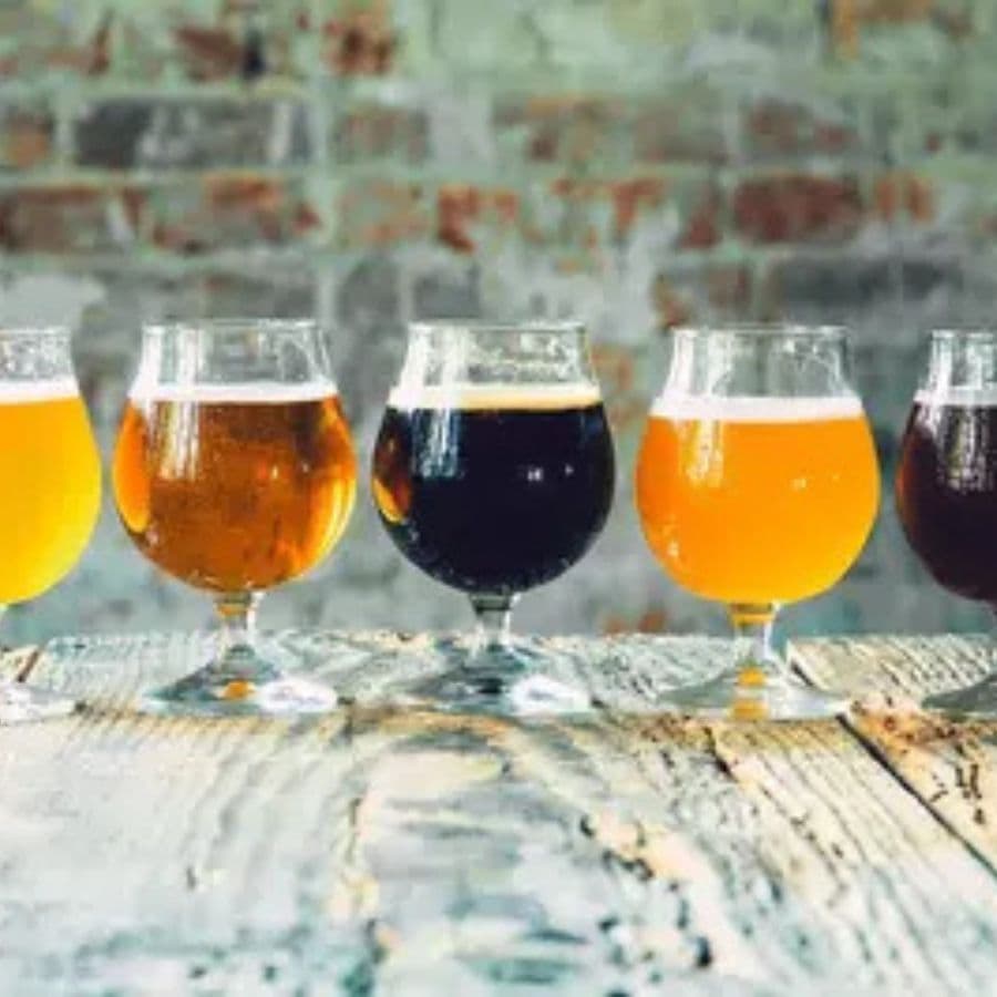 Five glasses of different colored beers are lined up on a rustic wooden table.