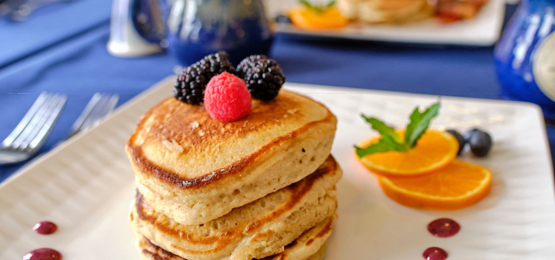 Stack of pancakes topped with berries and served with orange slices on a plate.