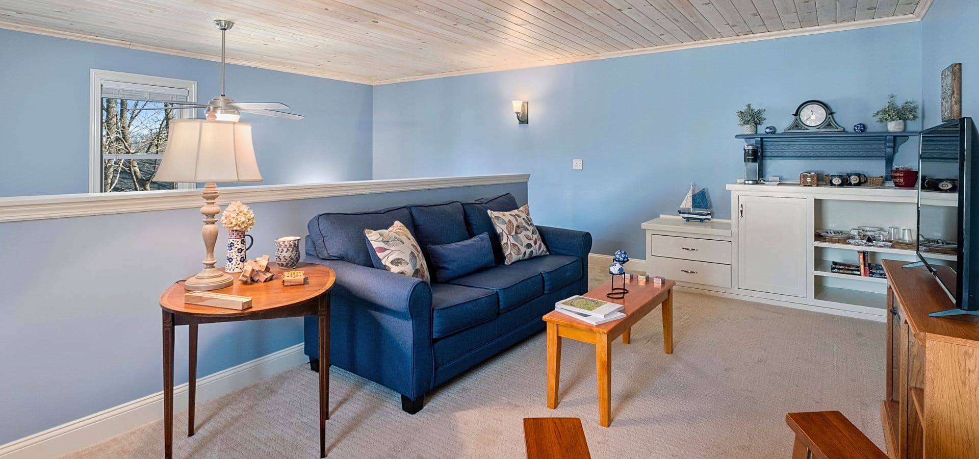 Bright, cozy living room featuring a blue couch, wooden furniture, and light blue walls.
