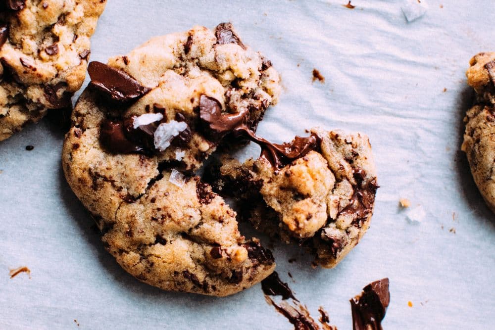 Close-up of a broken chocolate chip cookie on parchment paper.