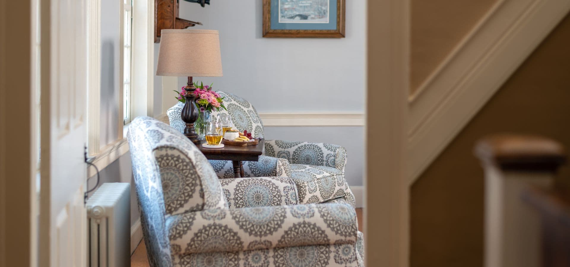 A cozy sitting area with patterned chairs, a lamp, a small table with drinks, and floral decor.