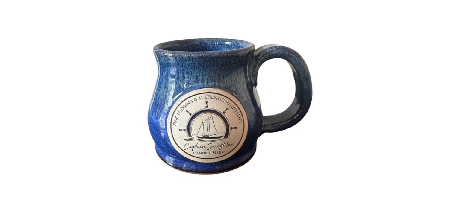 A blue ceramic mug with a round logo featuring a sailboat.