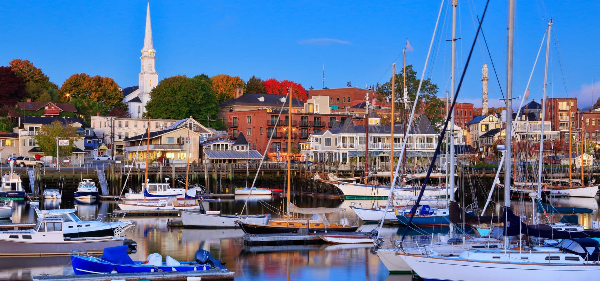 A harbor full of boats next to a small town with lots of trees in fall colors A harbor full of boats next to a small town with lots of trees in fall colors